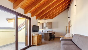 A modern interior with a wooden ceiling, a kitchen area, a grey sofa, and a sliding glass door leading to an outdoor space. - [Cotton Flower] Penthouse 15 minutes from Malpensa MXP (Busto Arsizio)