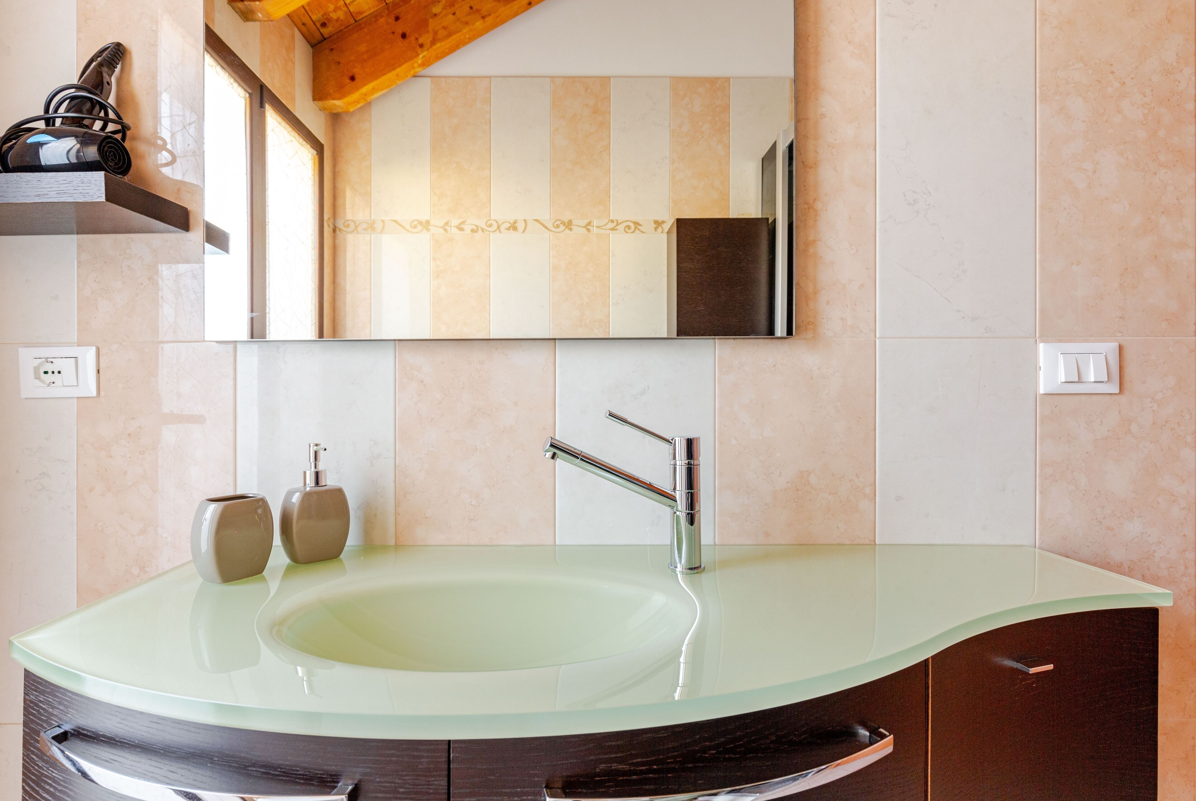 Een moderne badkamer met een glazen wastafel, een houten plank en een grote spiegel.