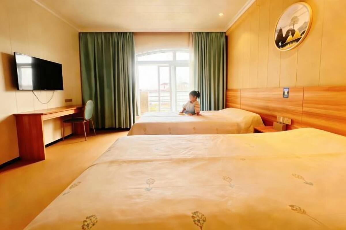 Habitación de hotel con dos camas, un escritorio, una silla, un televisor y una ventana con cortinas.