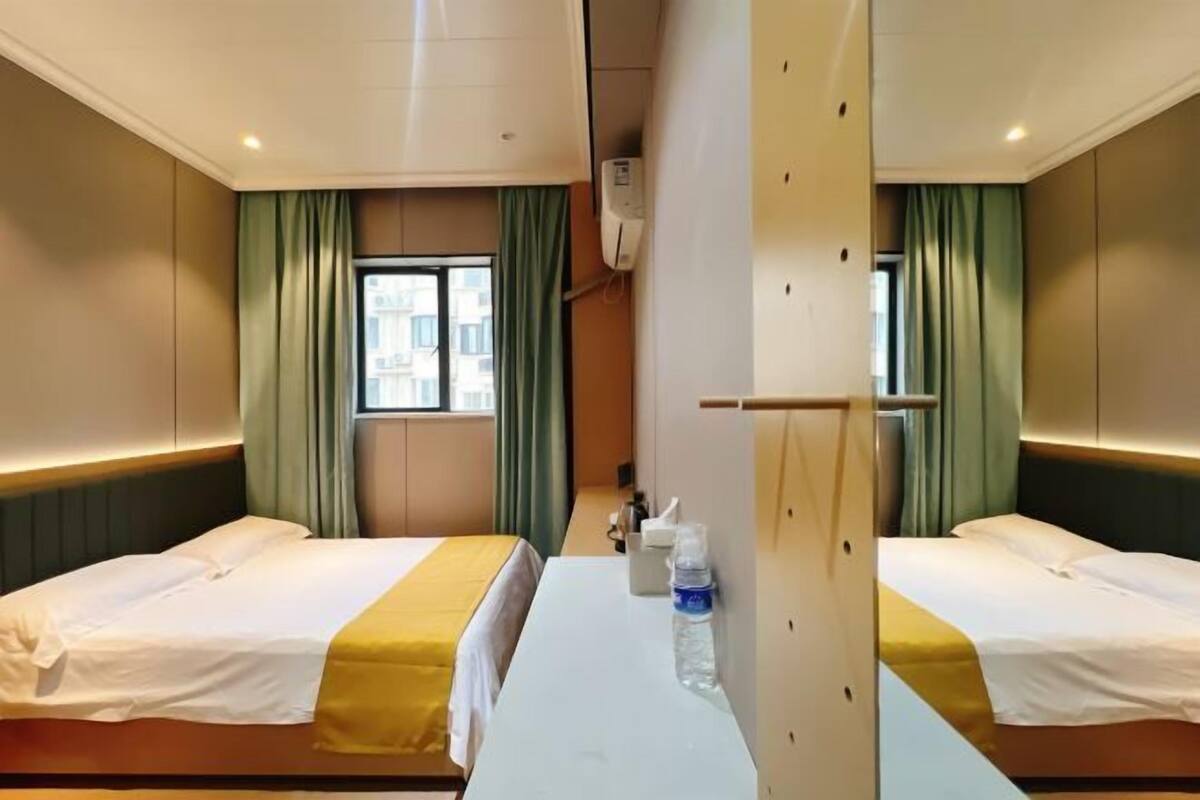 Habitación de hotel con dos camas, una mesa en el centro, una ventana y un espejo.