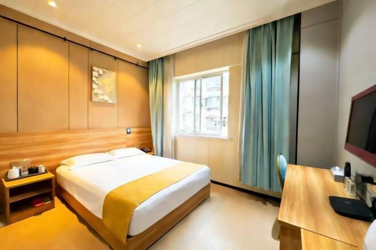 Una habitación de hotel con cama, mesita de noche, ventana y un escritorio con silla.