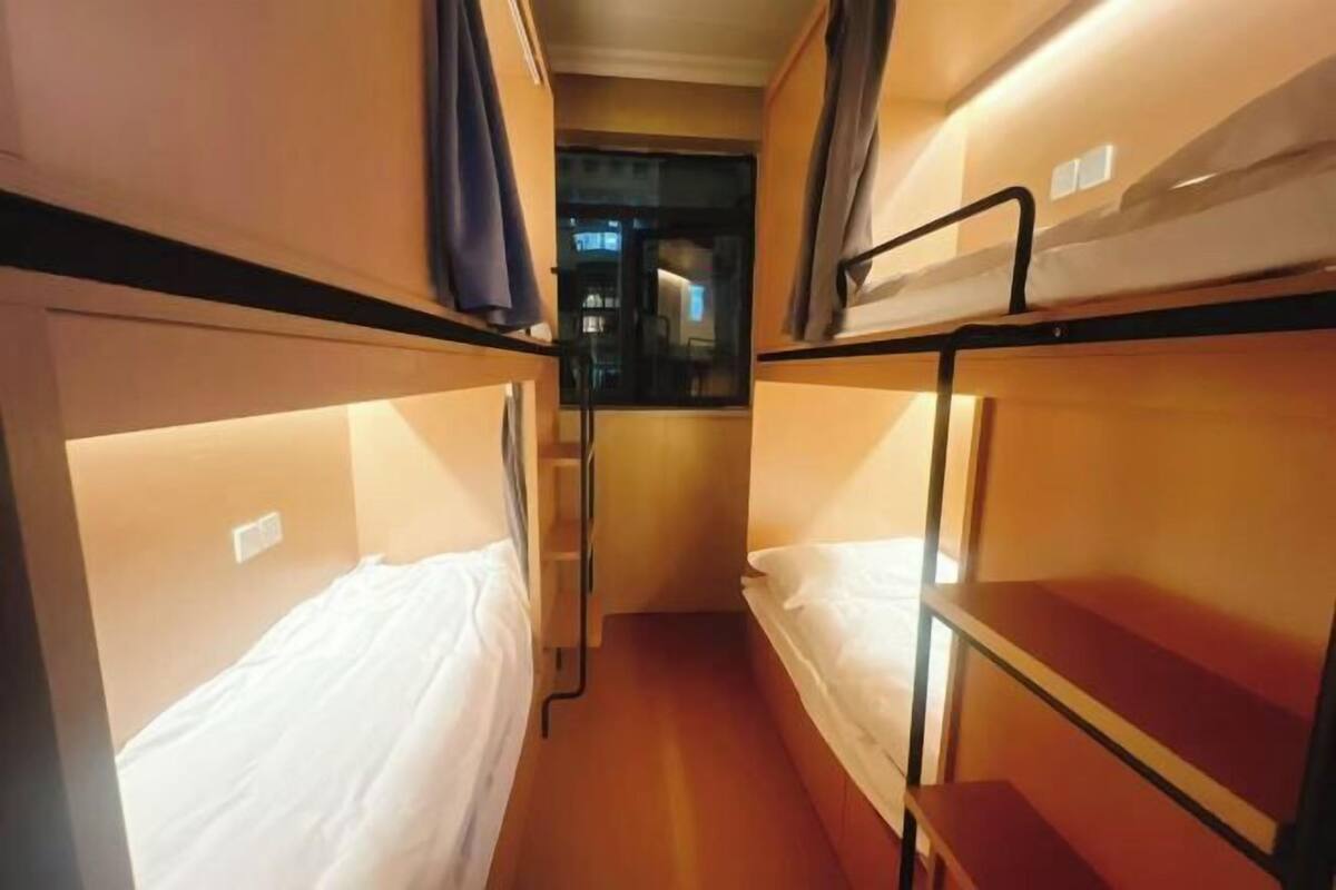 Un pasillo estrecho con literas a ambos lados, una ventana al final y una puerta que da a otra habitación.