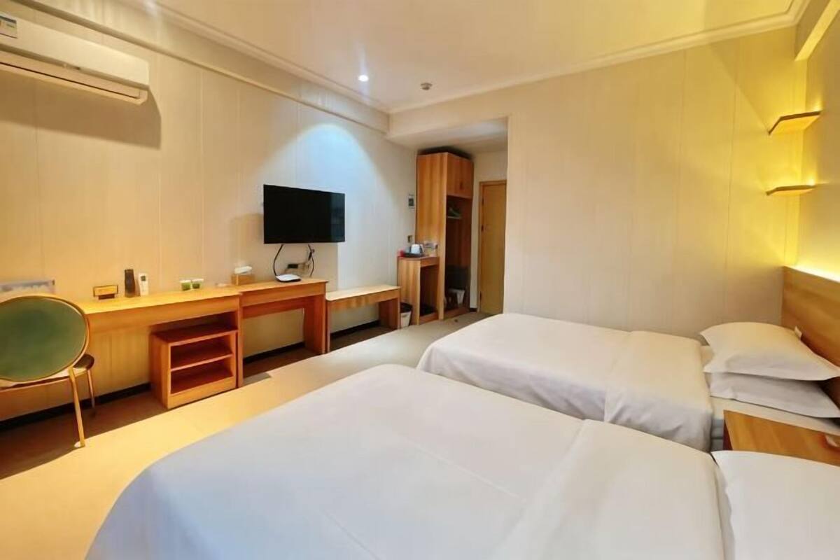 Una habitación de hotel con dos camas, un escritorio, una silla, un televisor y un armario.