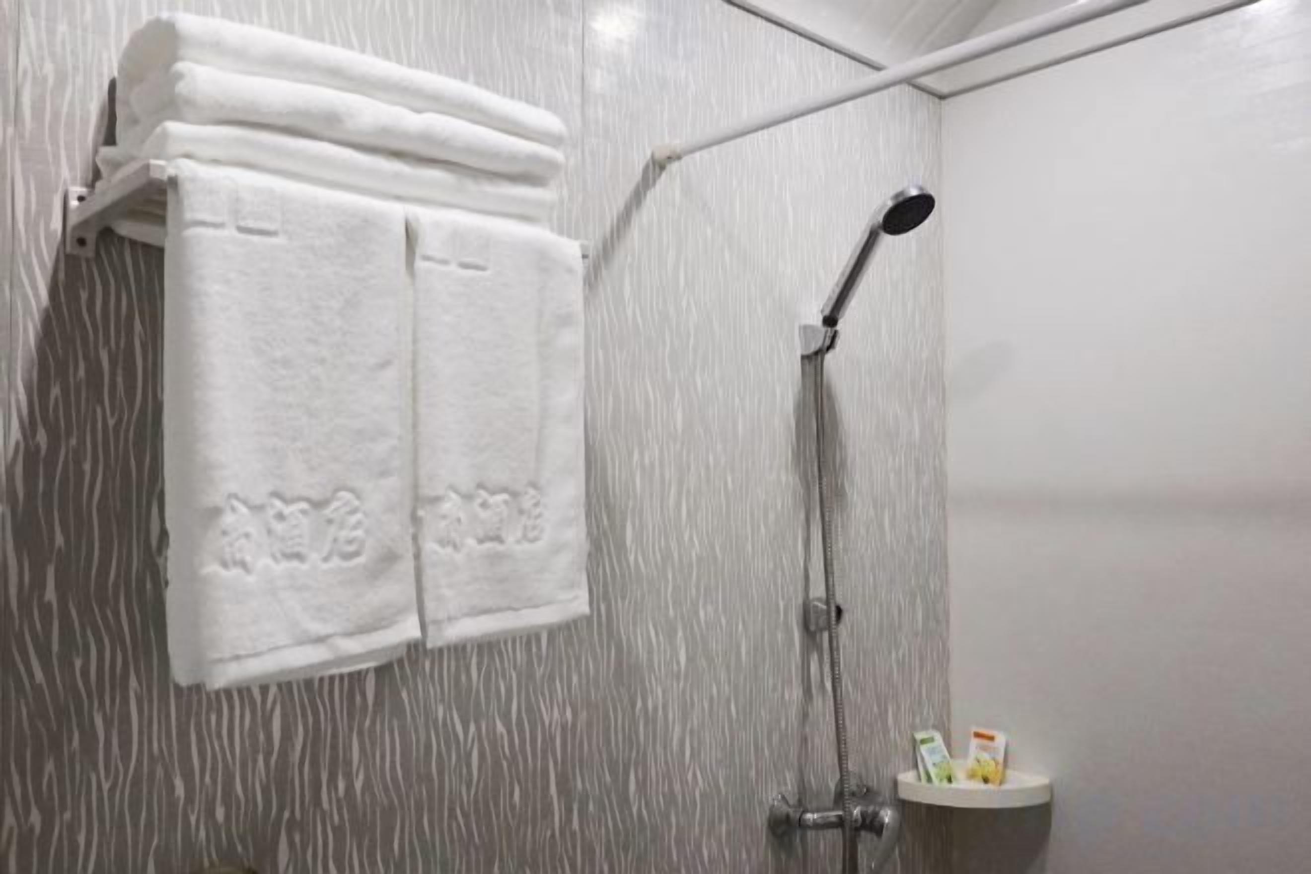 A shower with a handheld showerhead, a towel rack with folded towels, and a small shelf with toiletries.