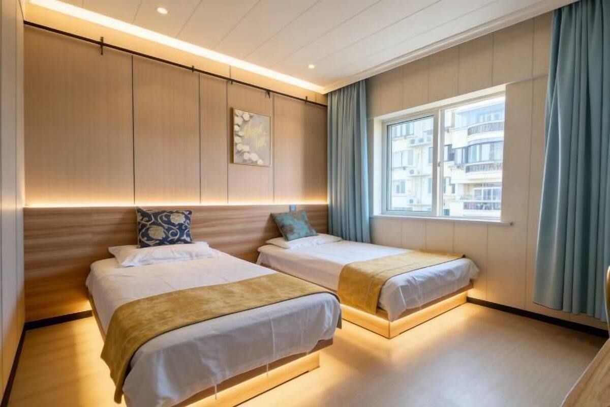 Habitación de hotel con dos camas, una ventana con cortinas, una obra de arte colgada en la pared e iluminación empotrada en el techo.