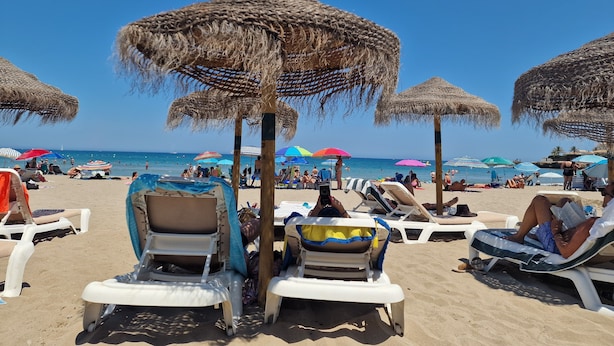 A beach with thatched umbrellas and lounge chairs.