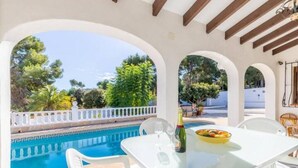 An outdoor pool area with a table and chairs, a bottle of champagne, and a bowl of fruit.