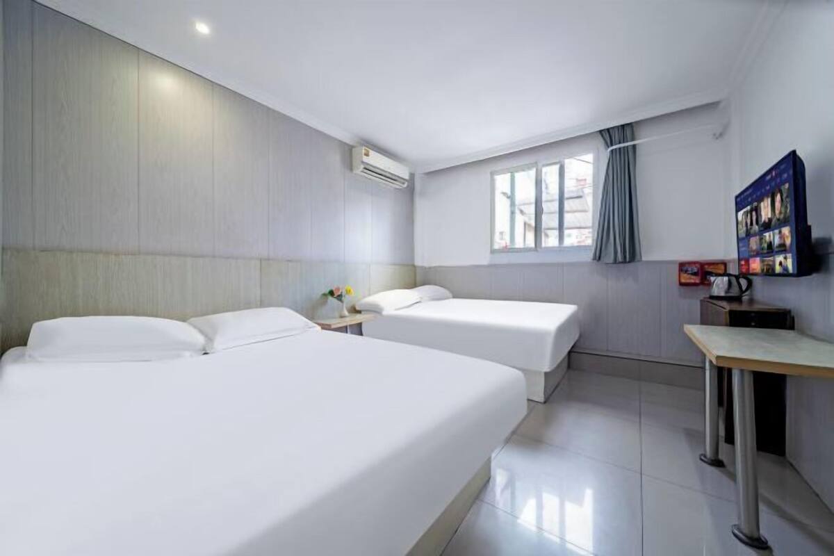 A hotel room with two beds, a small table, a TV, and a window with curtains.