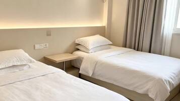 Quarto de hotel com duas camas de solteiro, uma mesa de cabeceira e cabeceira com iluminação embutida.