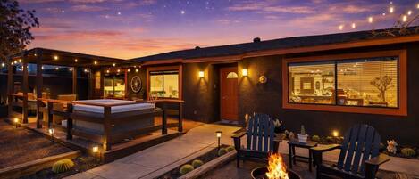 A modern outdoor patio with a fire pit, seating, and a view of the night sky.