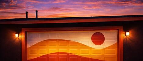 A garage door with a sunset view, two wall-mounted lights, and a metal trash can.