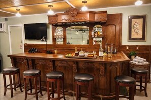 A bar area with a wooden bar counter, stools, and a variety of bottles and glasses. - The Rosemary House Joshua Tree (Joshua Tree)