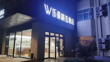 A hotel entrance with a prominent illuminated sign, glass doors, and a small outdoor area with plants.