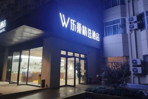 A hotel entrance with a prominent illuminated sign, glass doors, and a small outdoor area with plants. - Lechao Collection Hotel (Shanghai Bailian Central Zhenguang Road Subway Station) (Shanghai)