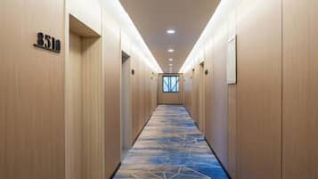 Un pasillo de hotel con paredes de madera, puertas de habitaciones numeradas y una alfombra estampada.