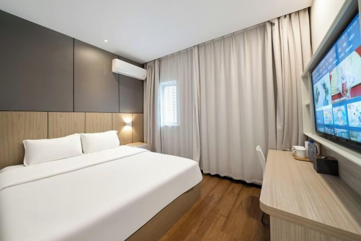 A hotel room with a bed, a desk, a TV, and a window with curtains.