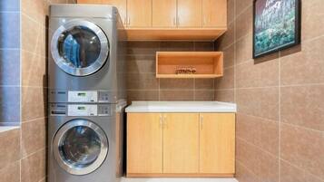A laundry area with stacked washing machines, wooden cabinets, and a shelf.