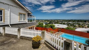 A white house with a balcony overlooking a swimming pool and a cityscape. - Napier Hilltop Stays (Napier)