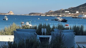 A poolside area with lounge chairs and a table, overlooking a coastal marina with boats and rocky terrain in the background. - ZELOS Guesthouse Milos (POLLONIAN)