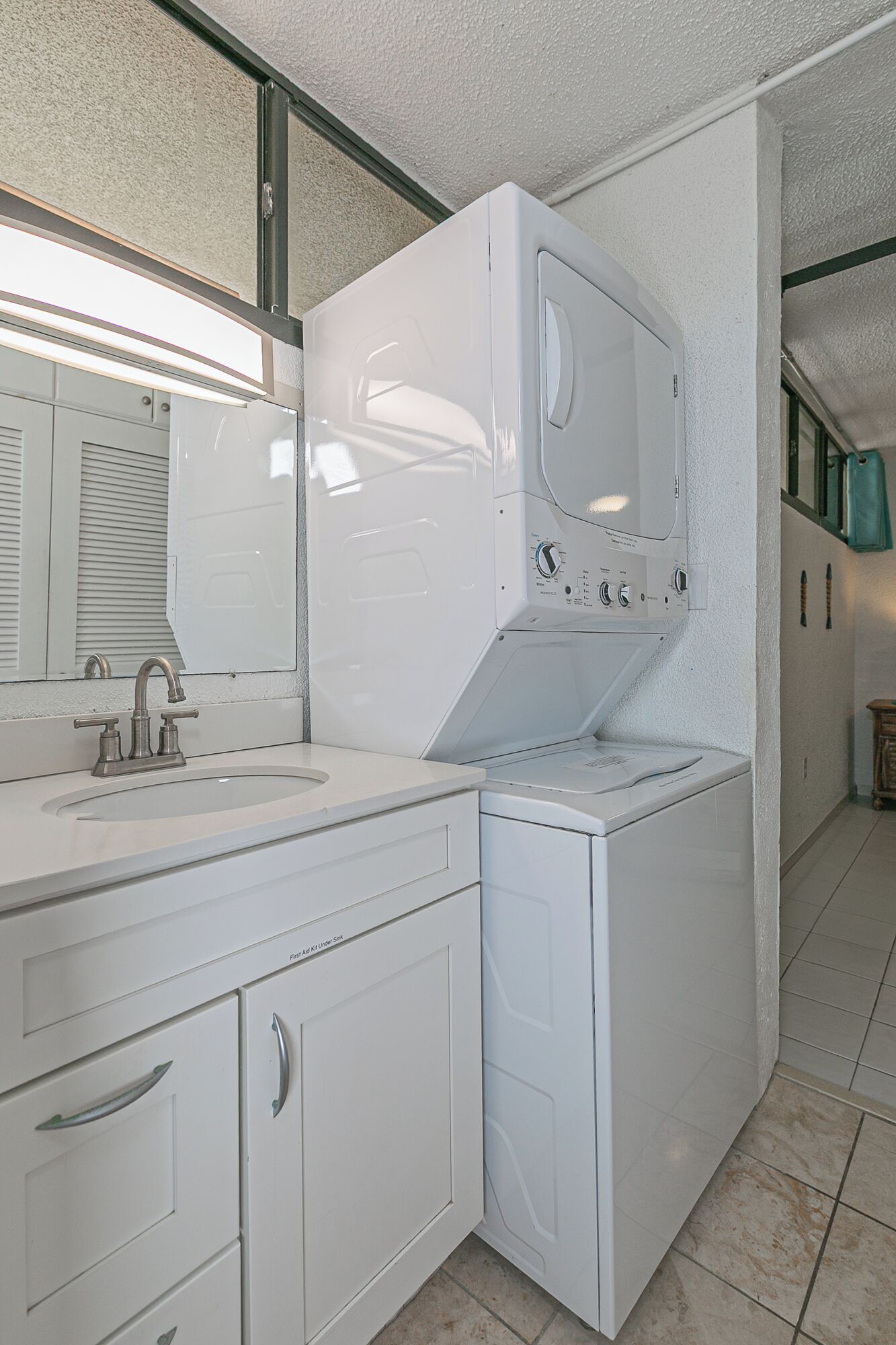 A compact bathroom with a white sink, mirror, and built-in washing machine.