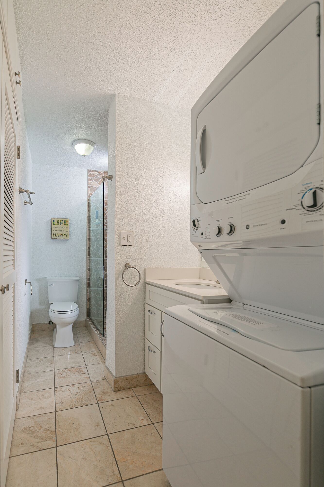 A compact bathroom with a toilet, a glass shower enclosure, and a washing machine.