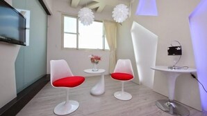 A modern room with two white chairs with red cushions, a small white table with a vase of flowers, and a white pedestal table with a lamp. - Tsai Hang B&B (Yilan)