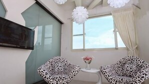 A modern room with a flat-screen TV, two leopard print chairs, a small table with a vase, and a large window with curtains. - Tsai Hang B&B (Yilan)