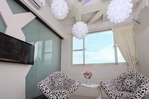 A modern room with a flat-screen TV, two leopard print chairs, a small table with a vase, and a large window with curtains. - Tsai Hang B&B (Yilan)