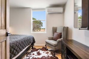 A bedroom with a bed, a chair, a cowhide rug, a window with a view, and an air conditioning unit. - Carmel in the Sky in Leakey (Leakey)
