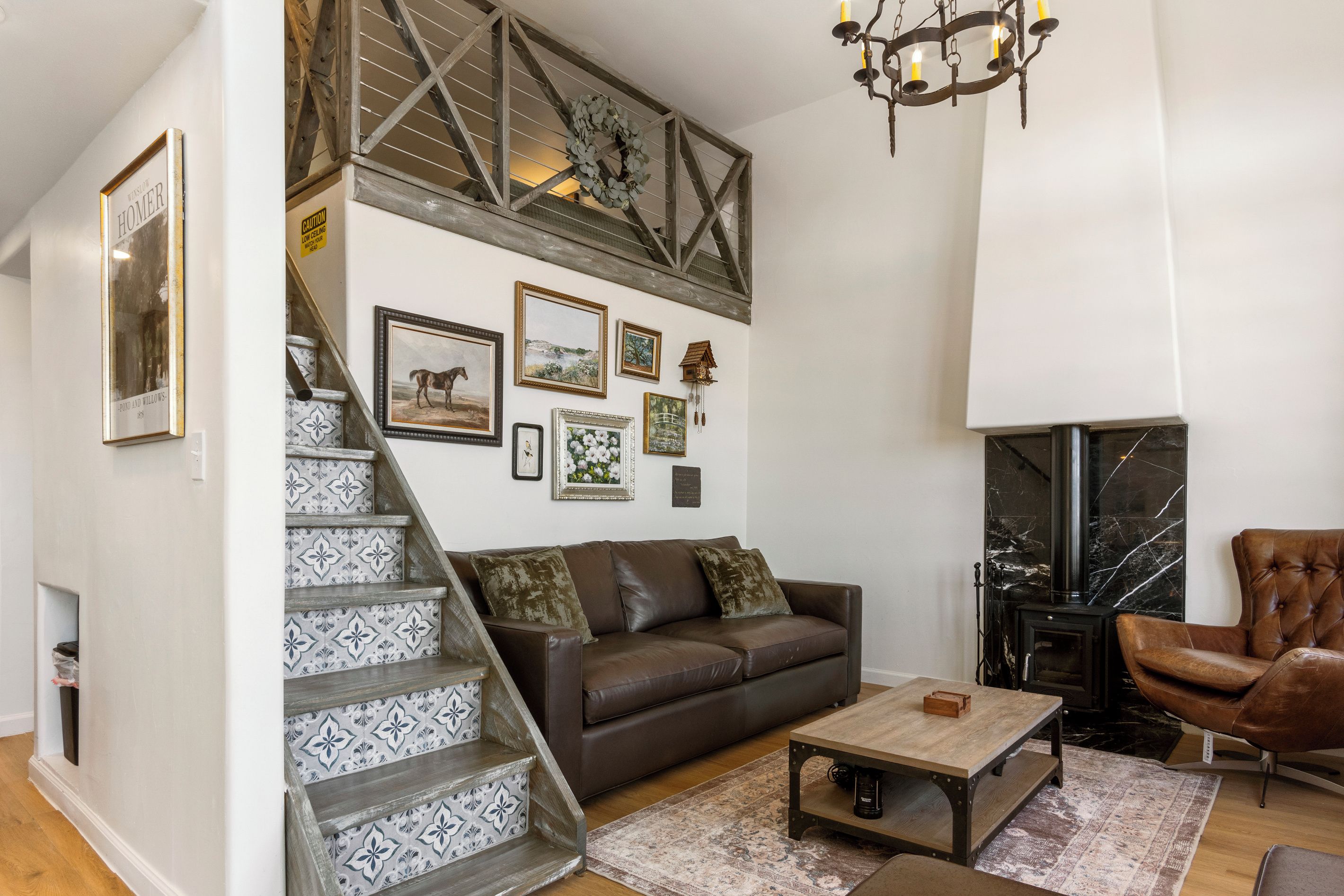 A living room with a brown leather sofa, a coffee table, a fireplace, and a staircase with patterned tiles.