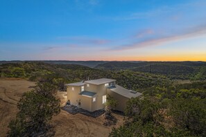 A modern two-story building with a flat roof, surrounded by a natural landscape with hills and sparse vegetation. - Carmel in the Sky in Leakey (Leakey)