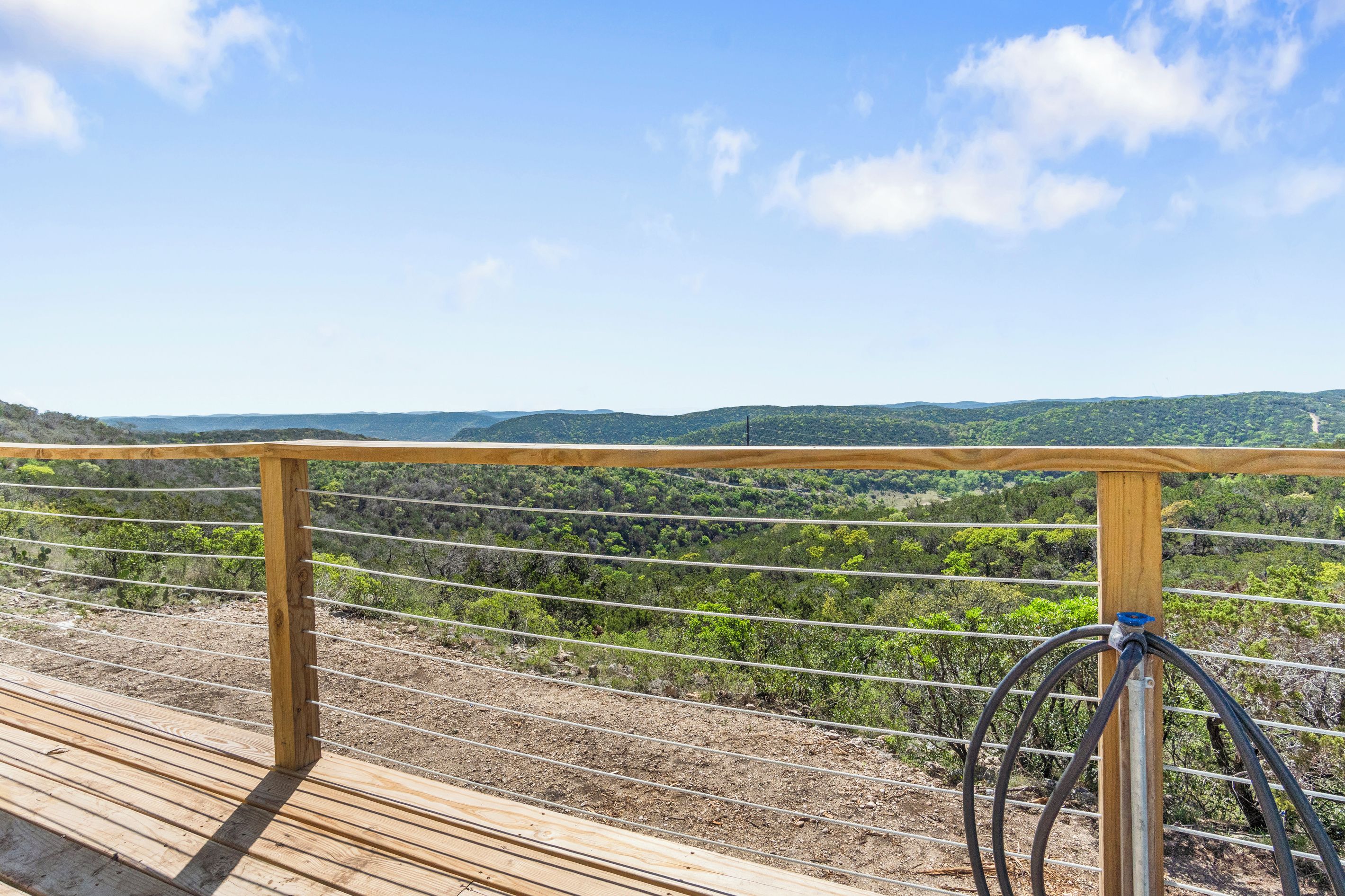A wooden deck with a metal railing overlooking a hilly landscape.