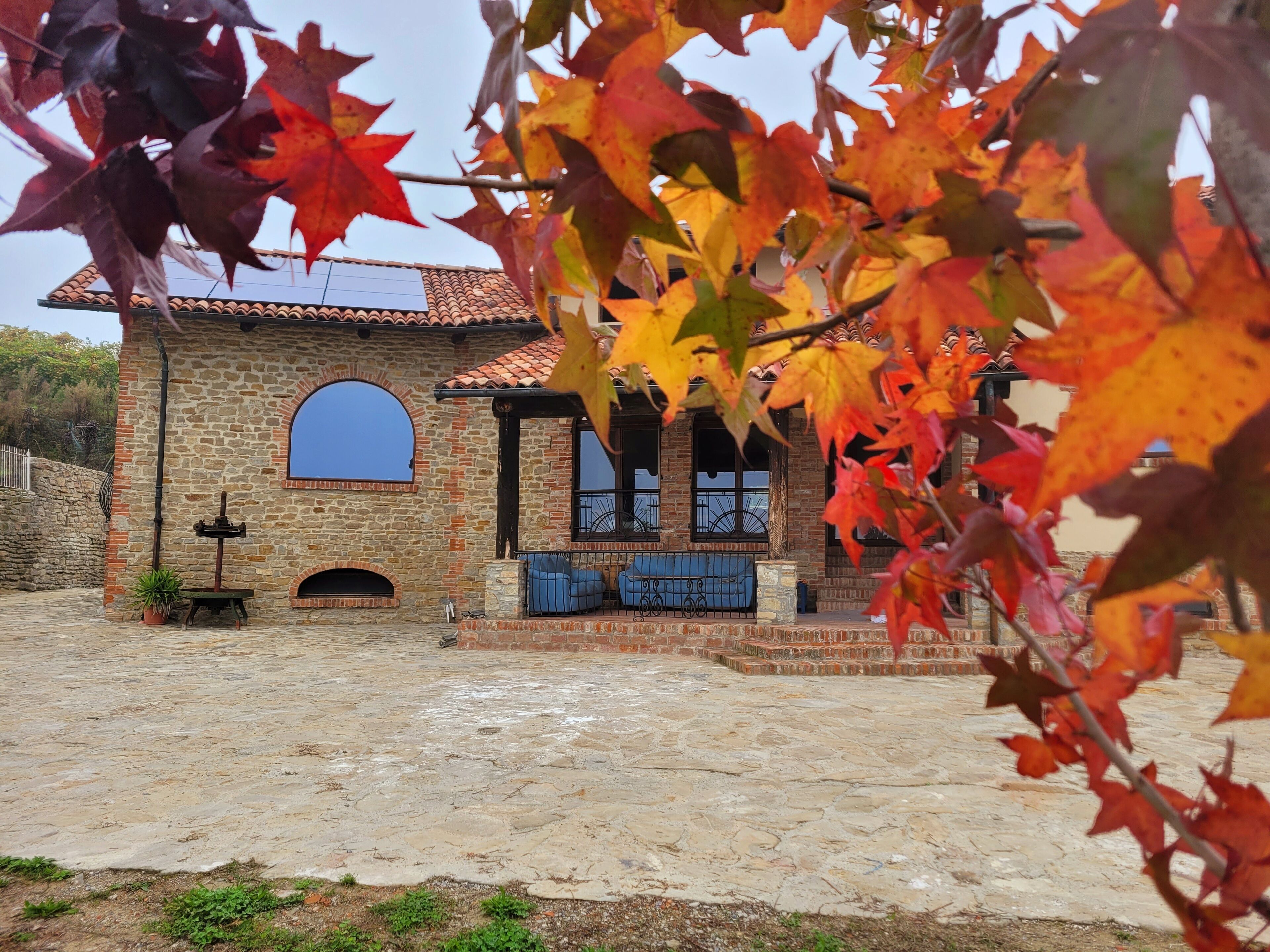 A stone building with a tiled roof, a large arched window, and a small porch with blue seating.