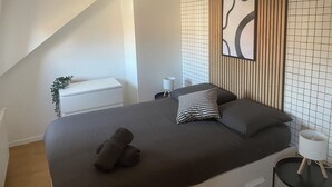 Et moderne soveværelse med en stor seng, en hængende lysarmatur, et sengebord med lampe og en dekorativ vægpanel.