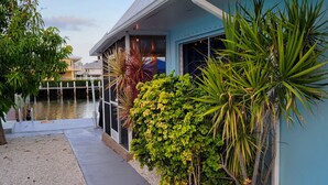 A waterfront property with a blue exterior, a gravel pathway, and various tropical plants. - Waterfront 2BR w/ Dock, Hot Tub & Easy Ocean Access – Boaters Welcome! (Marathon)