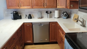 A kitchen with wooden cabinets, a dishwasher, a coffee maker, and a sink. - Waterfront 2BR w/ Dock, Hot Tub & Easy Ocean Access – Boaters Welcome! (Marathon)