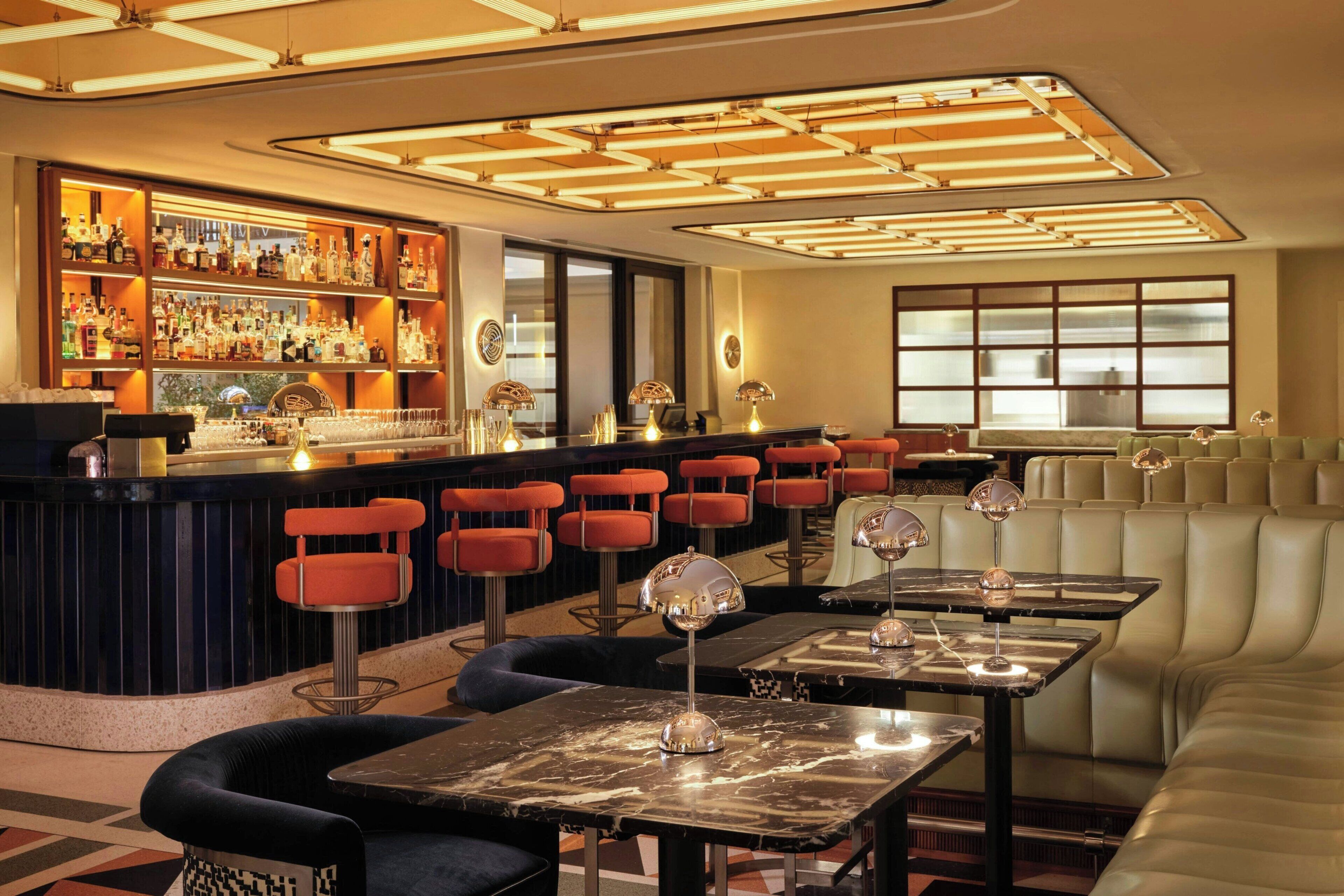 A bar area with a bar counter, multiple stools, and tables with bar lamps.