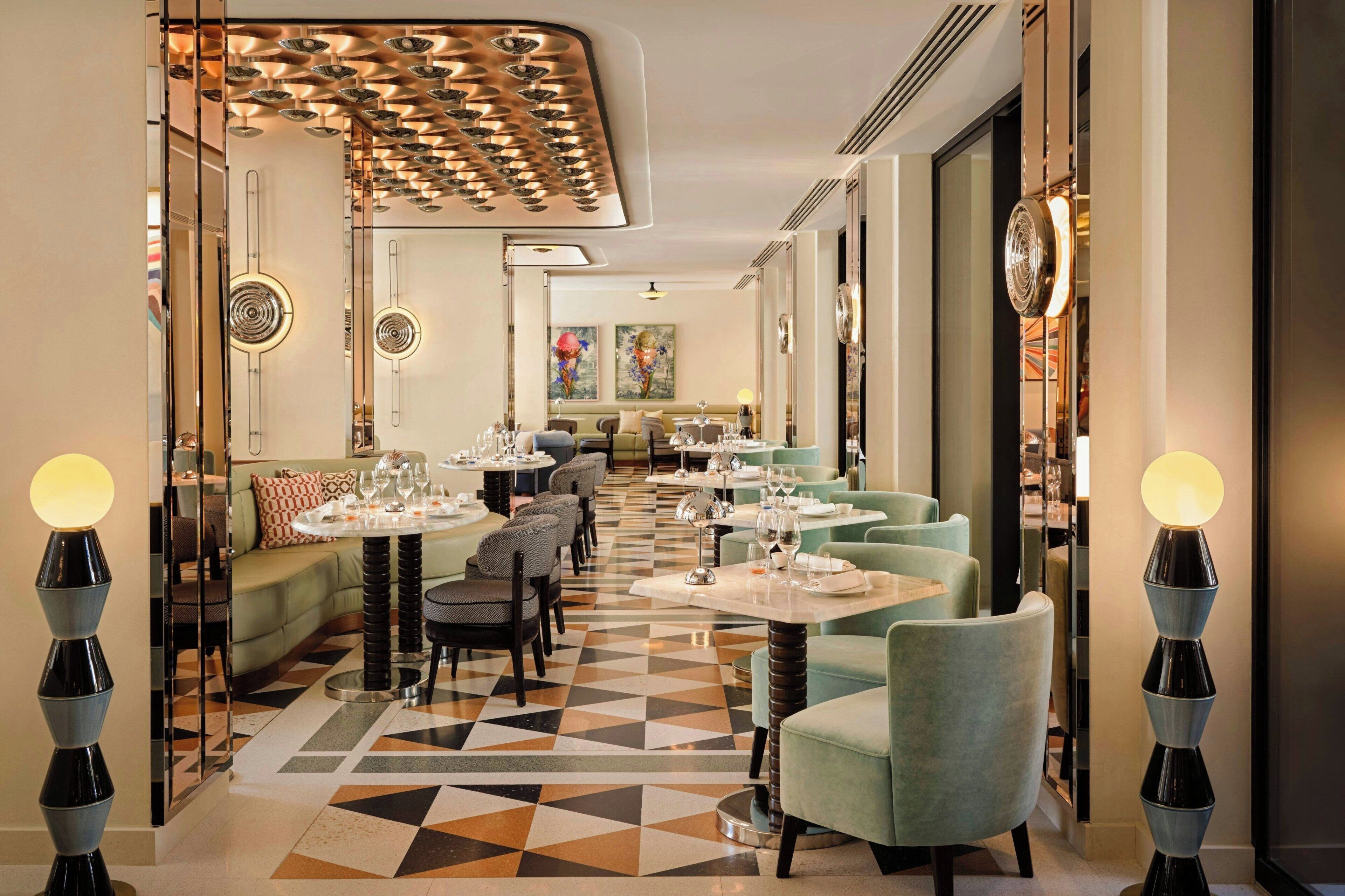 Ein Restaurant mit geometrischem Fußboden, runden Tischen mit Stühlen und modernen Leuchten.