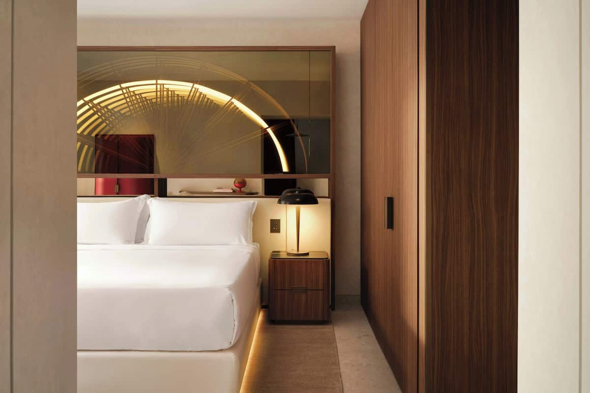 A hotel room with a bed, bedside lamp, and a wooden wardrobe.