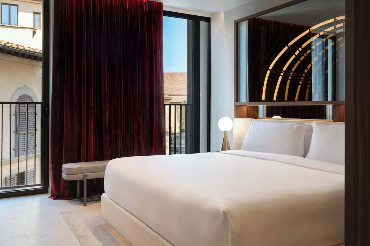 A hotel room with a large bed, a bench, a view of the outside, and a modern light fixture.