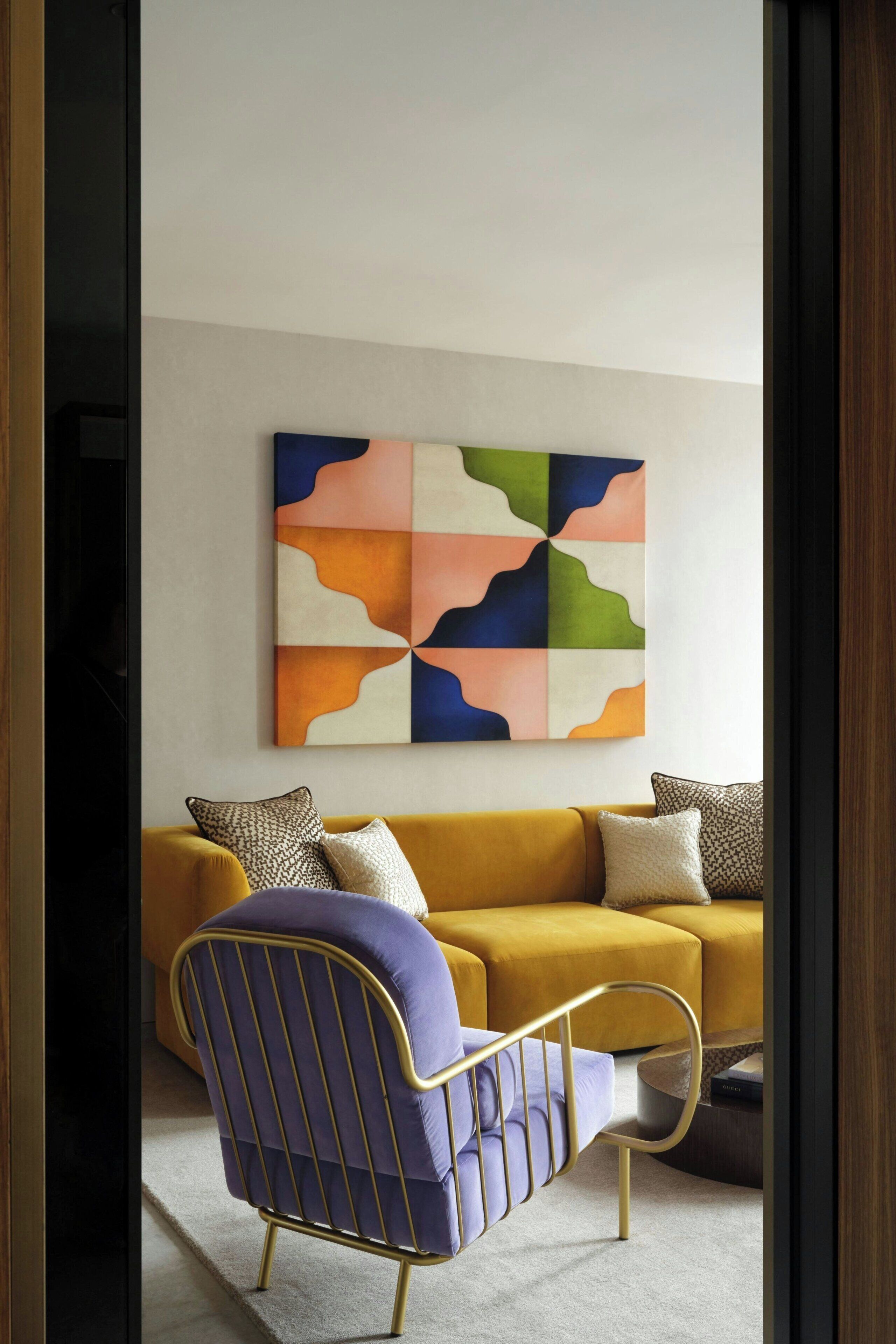 Un soggiorno moderno con un divano giallo, una poltrona blu e un quadro astratto dai colori vivaci appeso al muro.