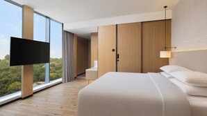A modern hotel room with a large bed, a flat-screen TV, a desk, and a view of the outdoors.