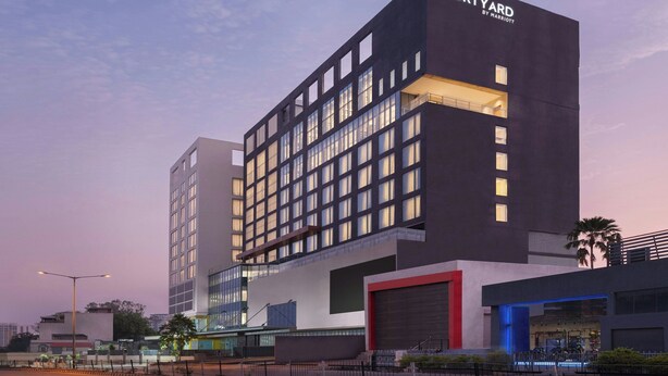 A modern hotel with a prominent 'Courtyard by Marriott' sign, featuring a large glass facade, multiple balconies, and a spacious entrance area.