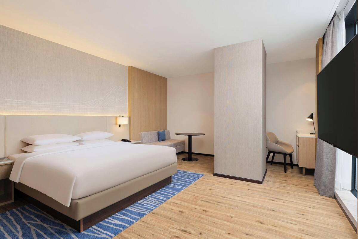 A modern hotel room with a large bed, a small sofa, a desk, and a TV.
