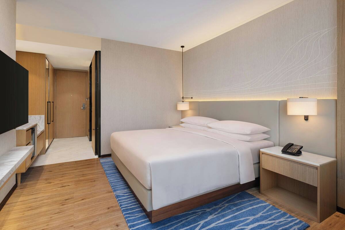 A hotel room with a large bed, bedside tables, a TV, and a wooden wardrobe.