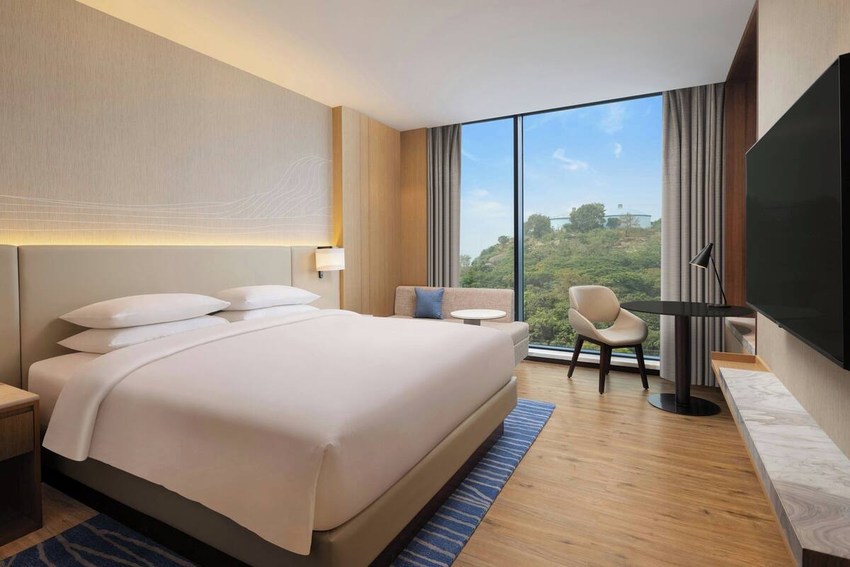 A modern hotel room with a large bed, a desk, a chair, and a TV.