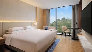 A modern hotel room with a large bed, a desk, a chair, and a TV.