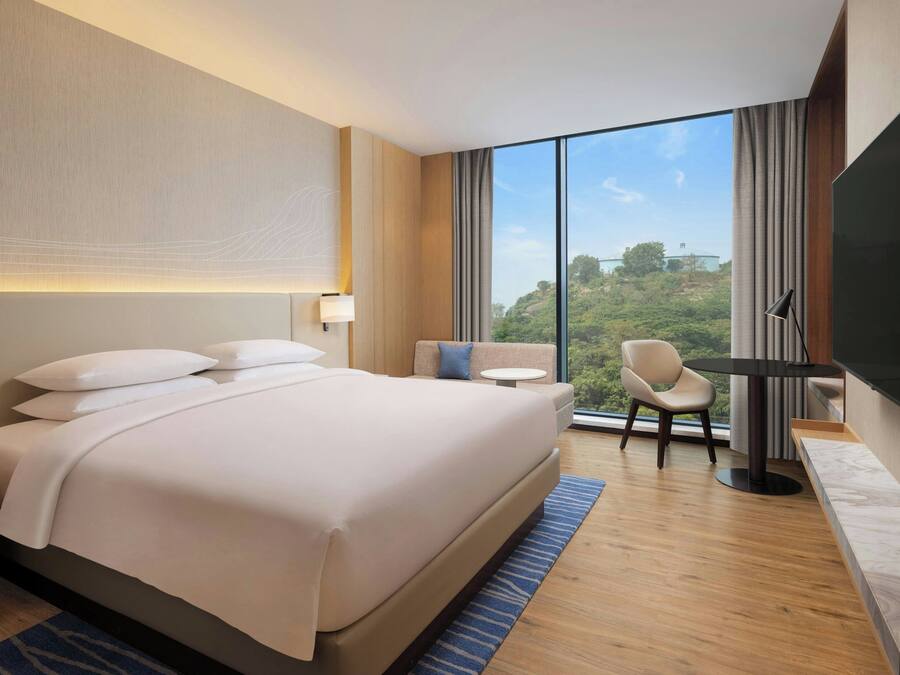 A modern hotel room with a large bed, a desk, a chair, and a TV.