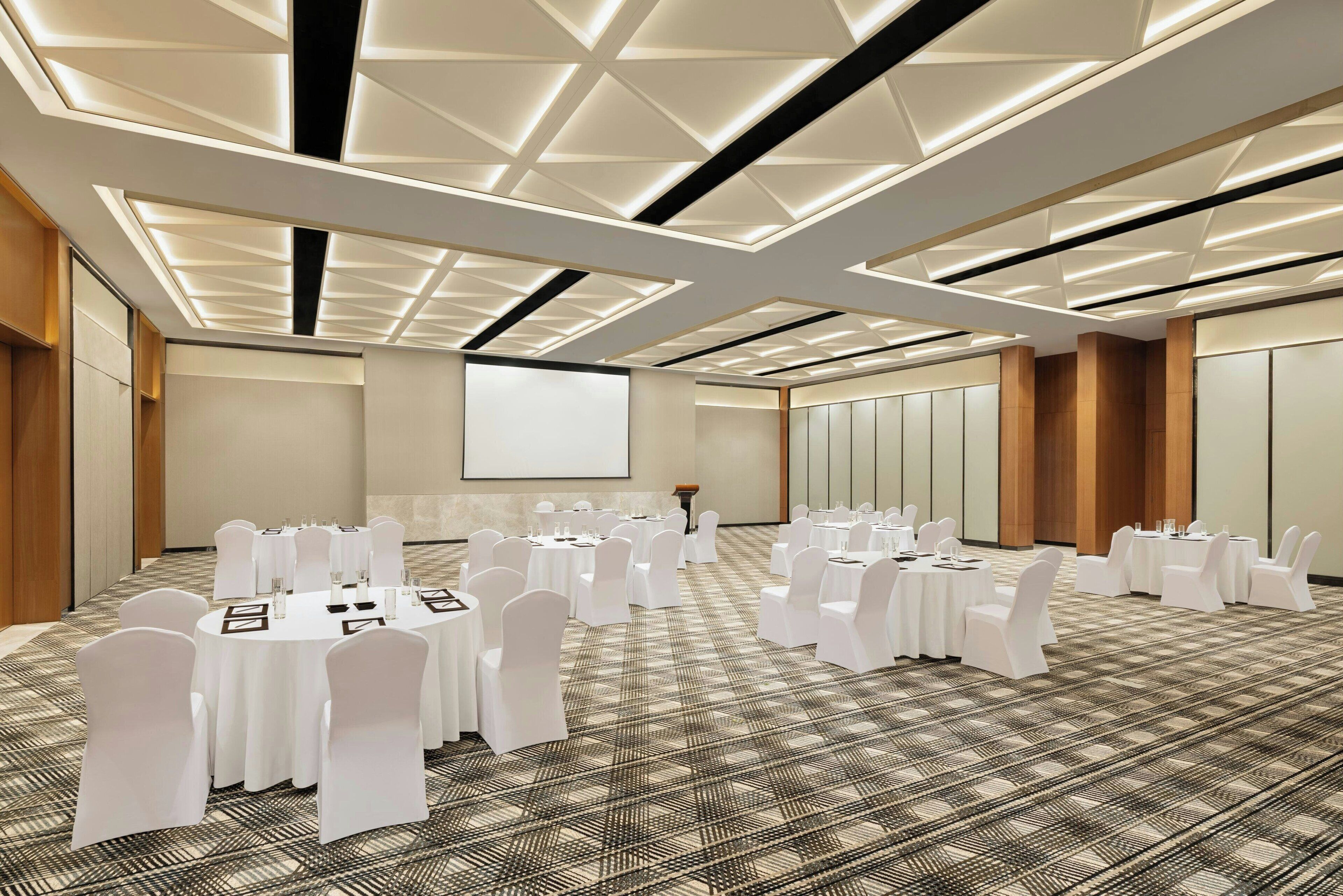A conference room with round tables, white chairs, and a large screen.