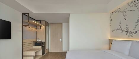 Una habitación de hotel moderna con una cama, un escritorio integrado con una silla, un armario y un televisor montado en la pared.